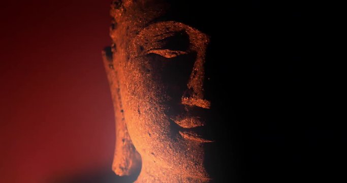 Calm and peaceful face of Buddha statue illuminated by candle light in darkness