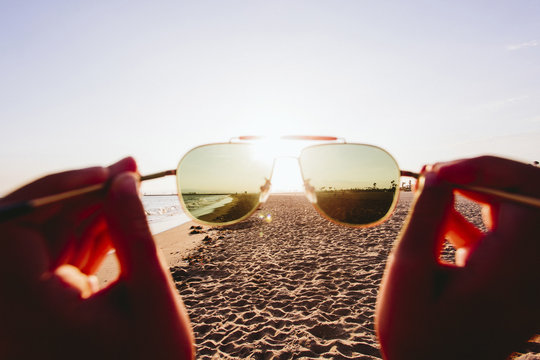 Cropped image of person holding sunglasses on beach during summer