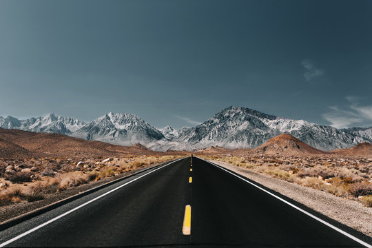 Empty road passing through desert landscape against blue sky