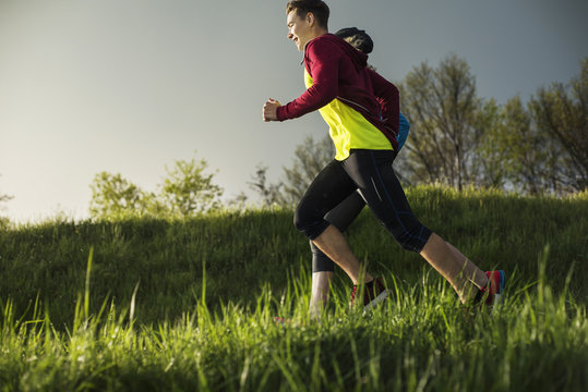 Side view of athletes running on grassy field during sunset