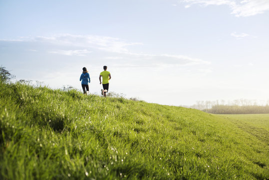 Rear view of couple running on grassy field against sky