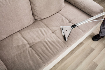 Person Cleaning Sofa With Vacuum Cleaner