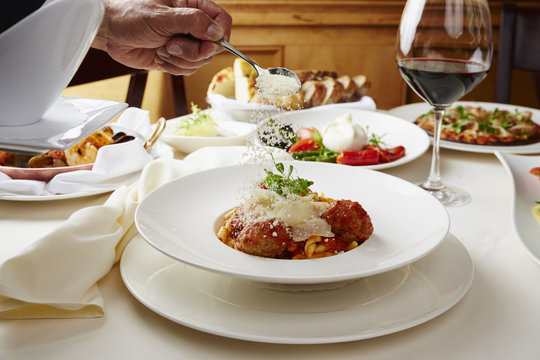 Chef pouring crushed parmesan cheese on meatballs and pasta at restaurant