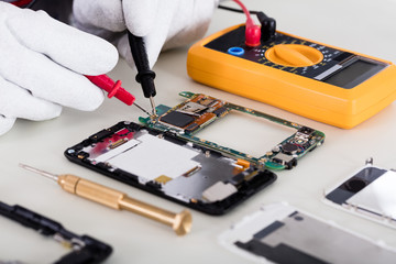 Person Checking Mobile Phone With Digital Multimeter