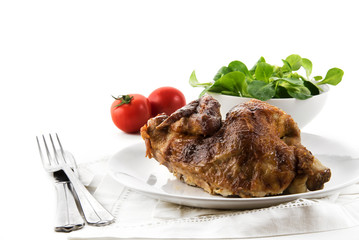 Half chicken, crispy grilled, with cutlery, salad and tomatoes against a white background