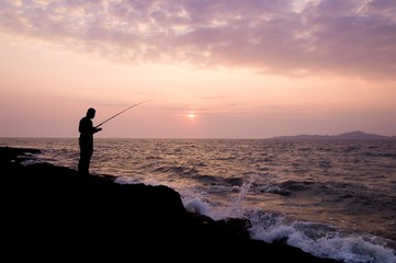 Silhouette of man fishing on the stone at seaside