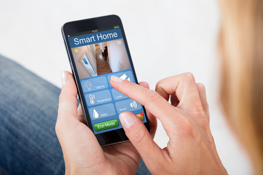 Person Holding Mobile Phone With Home Security System
