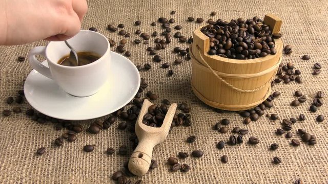 coffee that is sweetened and mixed by a female hand on jute with coffee beans in wooden bucket and wooden scoop