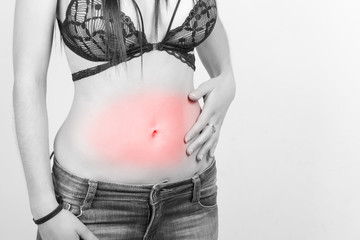 Woman in jeans and black bra, touching her waist with one hand, over a gray background. Black and...