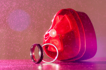 Red heart and wedding rings in the rain on pink light.