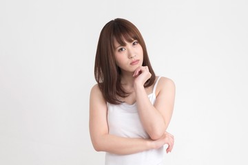 若い女性が、疑問や悩みがあるようなポーズをしています。この画像の背景は、白です。