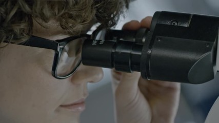 Extreme close up of female scientist in glasses observing sample with microscope 