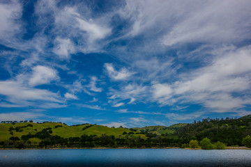 Fototapeta na wymiar White clouds on blue sky over green hills and lake