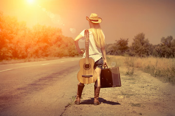 Young woman with guitar on the road and her vintage baggage