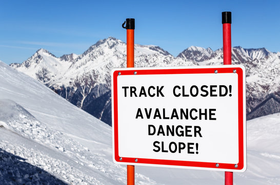 No skiing track closed avalanche danger slope. Security interdiction sign with black text on white background in red frame against snowy winter mountain peak and blue sky