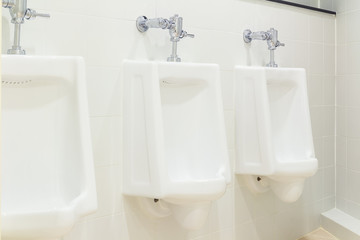 Row of white urinal for men on tile wall in toilet.