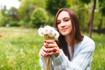 Pretty girl blowing dandelion in summer park. Green grass and beautiful nature