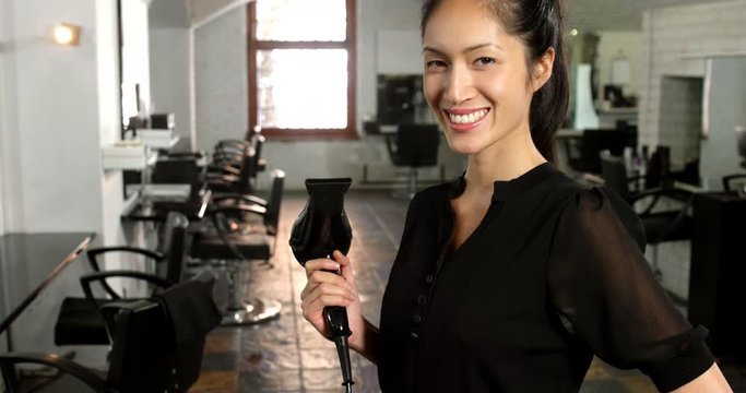 Smiling female hairstylist holding hair dryer in hair salon