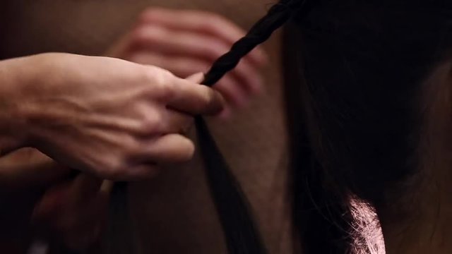 Hairdresser makes hairstyle for the model close-up. Preparing for the fashion show. Dressing room for models. Weaving hair braids.