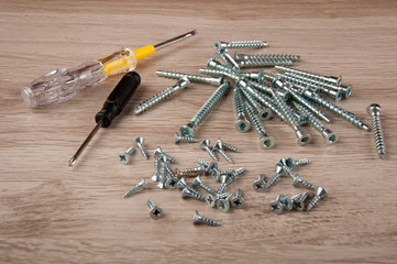 Two screwdrivers and matallic screws lay on wooden table