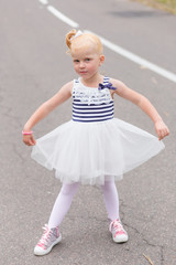Fototapeta premium A cute little girl in a beautiful dress and sneakers playing on
