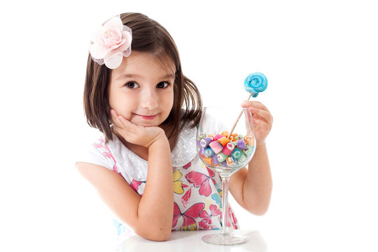 Pretty girl among the sweets, candies and lollipops. Funny child with candy lollipop, happy little girl eating big sugar lollipop, kid eat sweets. surprised child with candy. 