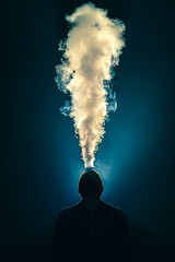 The man smoke an electronic cigarette against the background of bright light - obrazy, fototapety, plakaty
