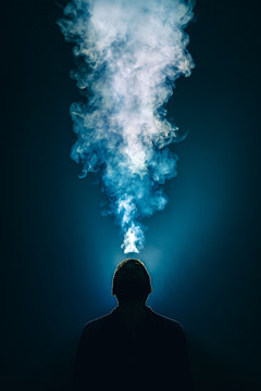 The man smoke an electronic cigarette on the background of bright light