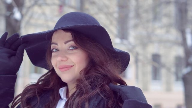 Young business girl walking in the winter city in black clothes and big hat.