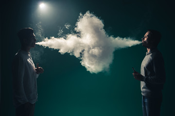 The two man smoke an electrical cigarette on the dark background