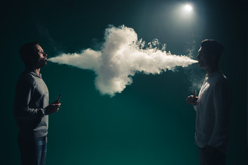 The two man smoke an electrical cigarette on the dark background