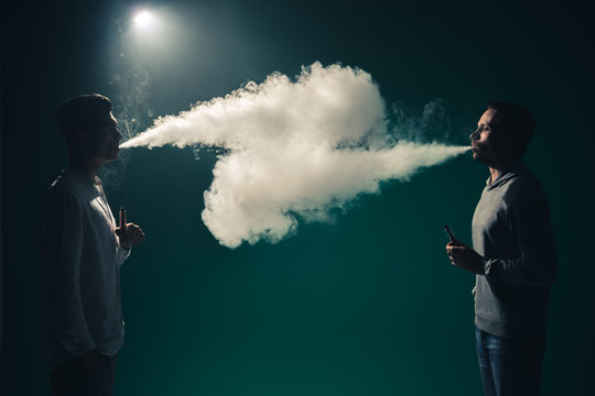 The two man smoke an electrical cigarette on the black background