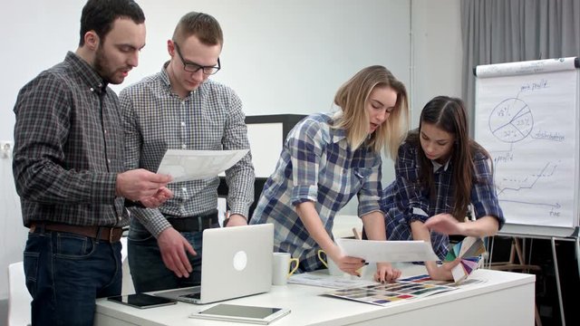 Two architects discussing layout while female coworkers looking at color palette