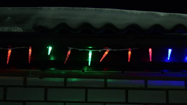 multi-colored Christmas lights decorate house at night, shining garland on winter roof, snow lies on roof
