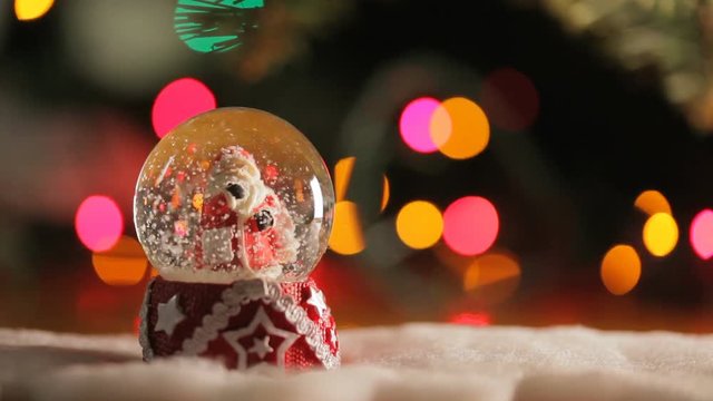 The figurine of Santa Claus in a glass bowl on a background of Christmas lights