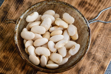 Sifter or mesh strainer with wet white beans on a wooden board.