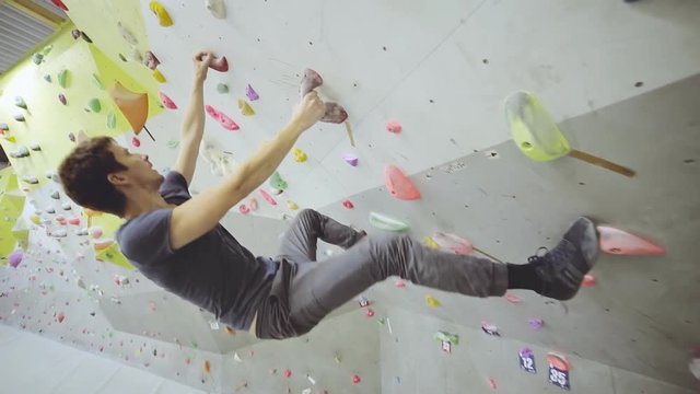Free climber fit man on artificial climbing wall rock in color bouldering gym