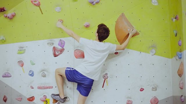 Free climber boy on artificial climbing wall rock in color bouldering gym