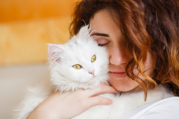 Cute girl with curly hair hugging white fluffy cat
