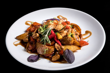 Fried potatos with vegetables and pork in white plate. Isolated on black background
