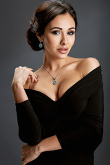 Fototapeta premium Beautiful woman standing in a black dress over gray background