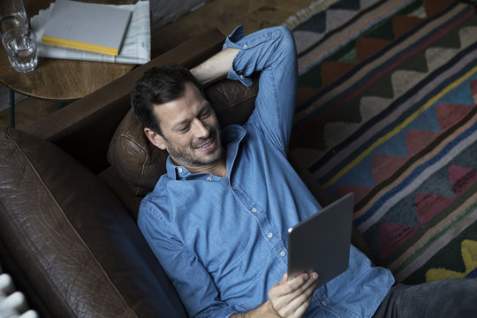Man lying on couch, using digital tablet