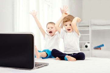 Two joyful boys, sitting in front of a laptop screen in the children's room