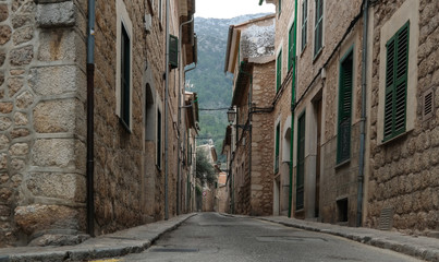 Fototapeta na wymiar low angle shot of empty narrow street in Soller Mallorca with typical historic houses on both sides and mountains in far distant background