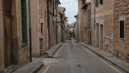 motorcyclist riding down empty narrow street in Soller Mallorca with typical historic houses on both sides and mountains in far distant background
