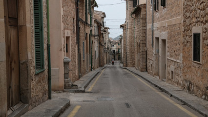 Fototapeta premium motorcyclist riding down empty narrow street in Soller Mallorca with typical historic houses on both sides and mountains in far distant background