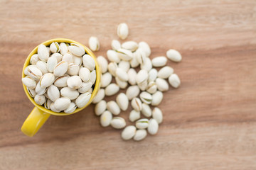 Yellow bowl of pistachios on wooden background