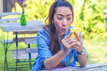 Beautiful girl sitting on chair in garden outdoor with surprise looking in mobile