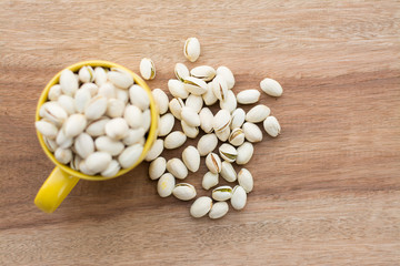 Yellow bowl of pistachios on wooden background