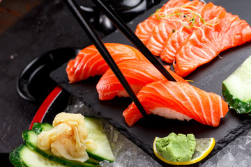Japanese cuisine. Salmon sushi and sashimi on a stone plate and ice and dark concrete background.